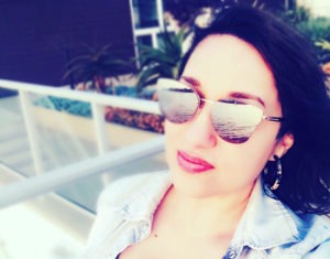 A selfie photograph of Laura Coronado, Communications Specialist at website design and development agency, WebDevStudios. She is wearing reflective sunglasses and slightly smiling at the camera.