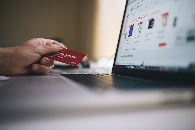 A photo image of a person shopping at their laptop while holding a credit card out.