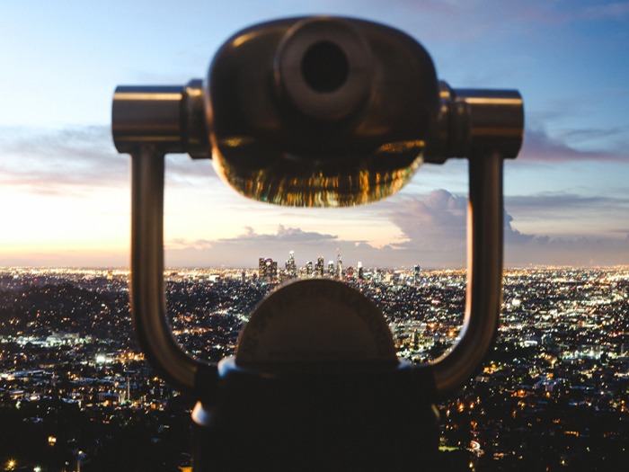 A photo image of a large telescope overlooking a city at dusk with the city lights twinkling in the background.