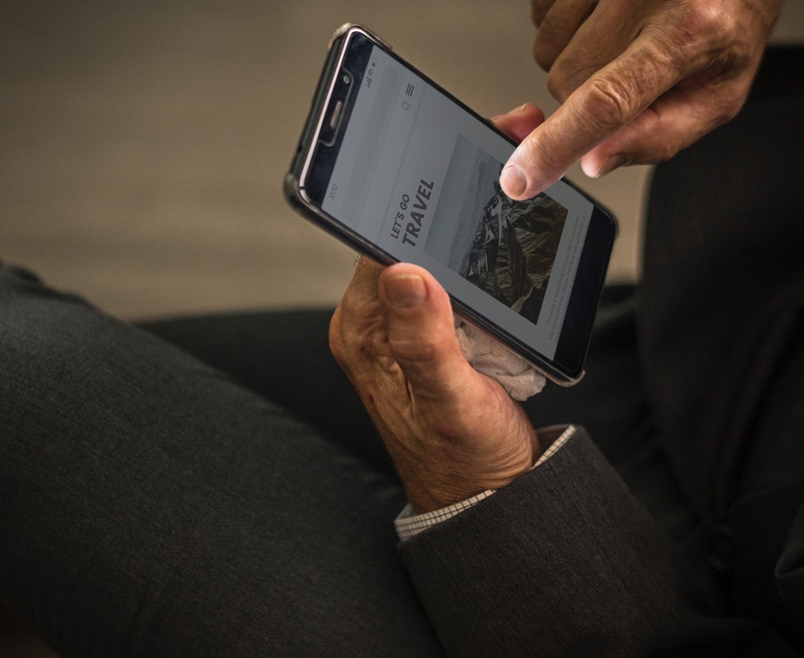 A photograph of a pair of hands holding an Android smartphone with one finger scrolling on the face of the phone with a website that says "Let's Travel" appearing on the screen used as an accompanying image for a blog post titled, "Web Design and Development Myths 2019 Edition."