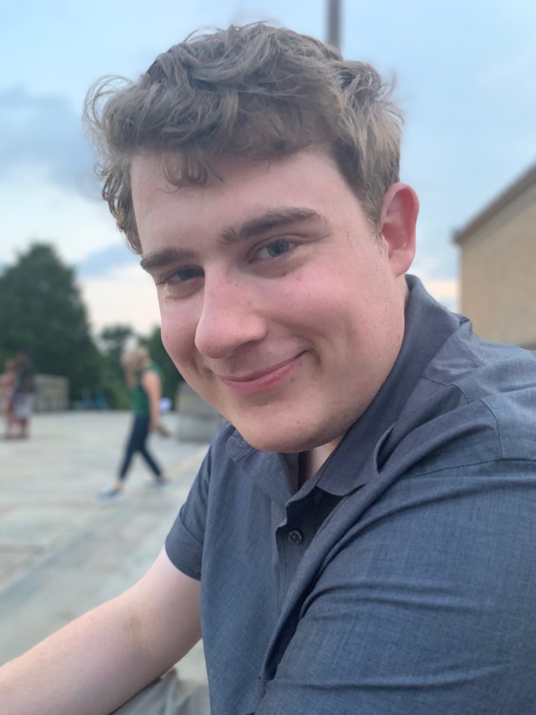 A portrait photo of George Gecewicz, Backend Engineer at WordPress website design and development agency WebDevStudios. George is photographed from the side, and he is turning his head to smile into the camera.