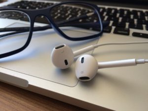 A photo image of a pair of glasses and ear buds resting on a computer keyboard and used as an accompanying image to emphasize the importance of listening to WordPress podcasts in order to learn more about WordPress.