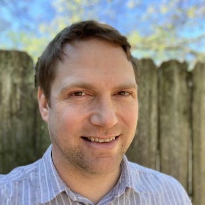 A photograph head shot of Marty O'Connor, a frontend engineer at WebDevStudios. He is smiling at the camera and is posed outdoors in front of a wood fence with a blue sky behind.