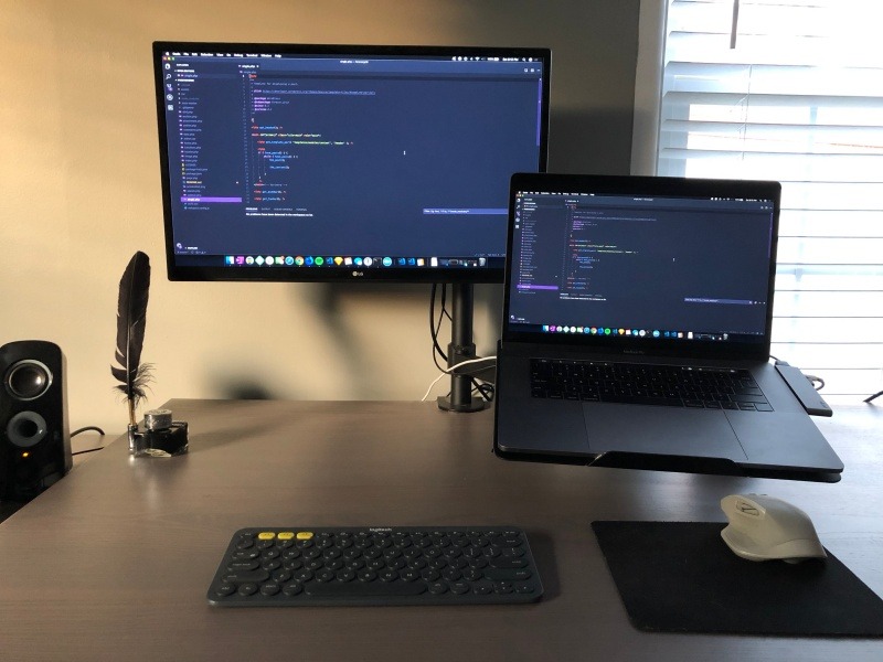 Monitor with Macbook Pro connected on mounting arms.