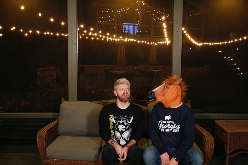 A photo image of WebDevStudios Lead Frontend Engineer, Corey Collins, sitting on a sofa with his eyes looking to his left and a disturbed look on his face, as someone else sitting next to him is wearing a horse head mask and looking at him, creepily. Corey is the author of the blog post, "Breaking the Cycle of the Mean Developer."