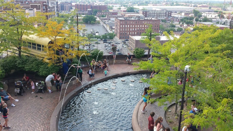 A photograph of the outdoor park at City Museum in St Louis, Missouri. People are gathered around the park's water fountain, which features water spouting.