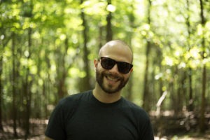A portrait of David Romsey, Backend Engineer at WebDevStudios. David is outdoors wearing sunglasses and facing the camera and smiling.