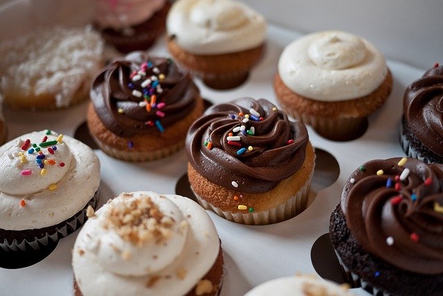 A photo of half a dozen of chocolate and vanilla cupcakes topped with sprinkles.