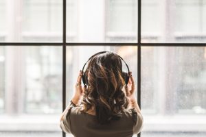 A photograph of the back of a woman's head as she looks out a window while wearing headphones.