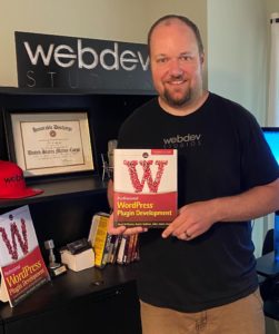 This is a photo of WebDevStudios CEO and co-author of Professional WordPress Plugin Development, 2nd Edition, Brad Williams, holding his book and smiling at the camera.