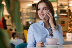 This is a photo of a woman on the phone and smiling. She has a cup of coffee with her.