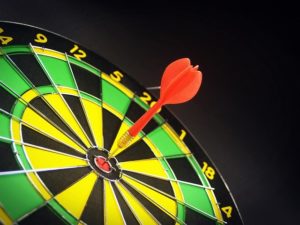A photograph of a yellow, green, and black dart board with a red dart in the center red bullseye.