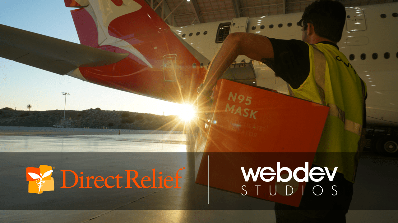 This is a photo image from Direct Relief that shows a person holding a box of N95 masks walking toward an airplane. This image is used for Team Science at WebDevStudios as they raise money for a charity challenge. It includes the Direct Relief and WebDevStudios logos.