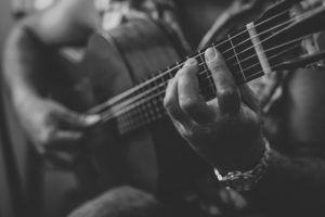 This is a black and white photograph of a person playing an acoustic guitar.