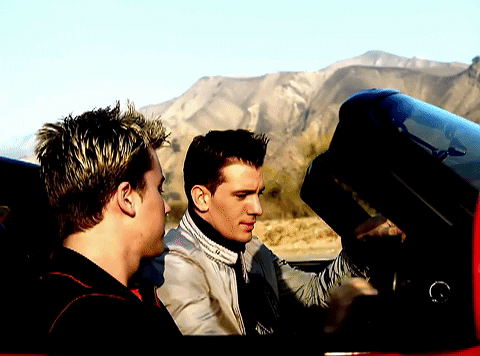 This is a GIF from an NSYNC video in which JC Chasez and Lance Bass are in a red convertible sports car and take off on a journey.
