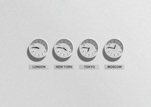 A photograph of four white clocks with black numbers and black hands hanging on a white wall. Each clock is set to a different time zone: London, New York, Tokyo, and Moscow.