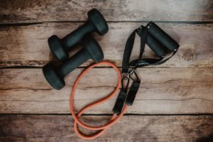 This is a flat lay, down angle photograph of resistance bands and a pair of hand weights sitting on a wood floor. 