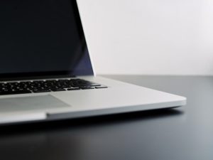 A photograph of an open Mac Book set atop a black desktop.