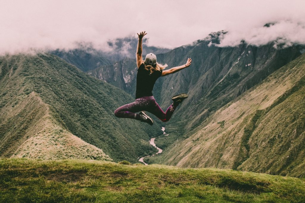 This is a photograph of a woman jumping with glee as she overlooks an Inca trail in Peru.