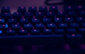 This is a close up photograph of a computer keyboard that is lit with purple light.