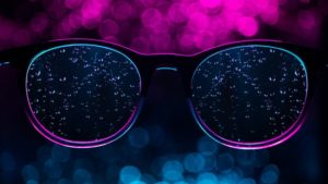 This is a close up photograph of a pair of eyeglasses that are speckled with rain drops and lit with purple light.