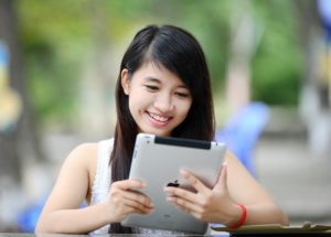 This is a candid photograph of a woman smiling as she reads the screen of her iPad.