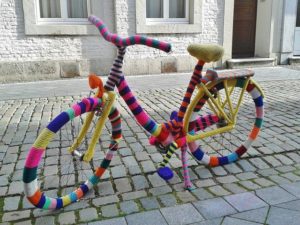 This is an outdoor photo of a bicycle wrapped in a many different colors of yarn.