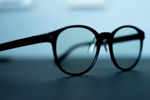 This is a photograph of a pair of black rimmed reading glasses sitting on a table.
