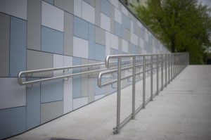 This is a photograph of a cement-paved outdoor wheelchair ramp with handrails.
