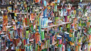 This is an interior photograph of a room filled with many used paint cans in a variety of sizes stacked on top of each other and on shelves, all with different colors of paint dripped and dried on the sides of the cans.