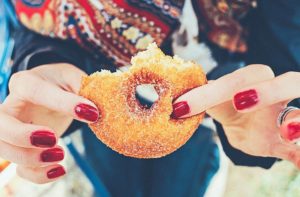 This is a photo of a pair of hands pinching the sides of a donut that has two bites take out of it.