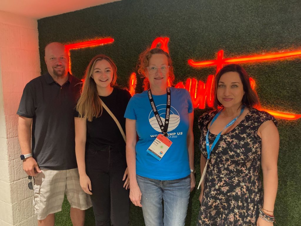 This is a photograph of WebDevStudios CEO, Brad Williams, Delivery Manager, Autry Reeves, Account Manager, Laura Byrne, and Marketing Strategist, Laura Coronado standing in front of a grass wall at WordCamp US.