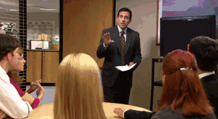 This is a GIF from the television show The Office of Michael standing at the front of a conference room while everyone listens and then cheers.