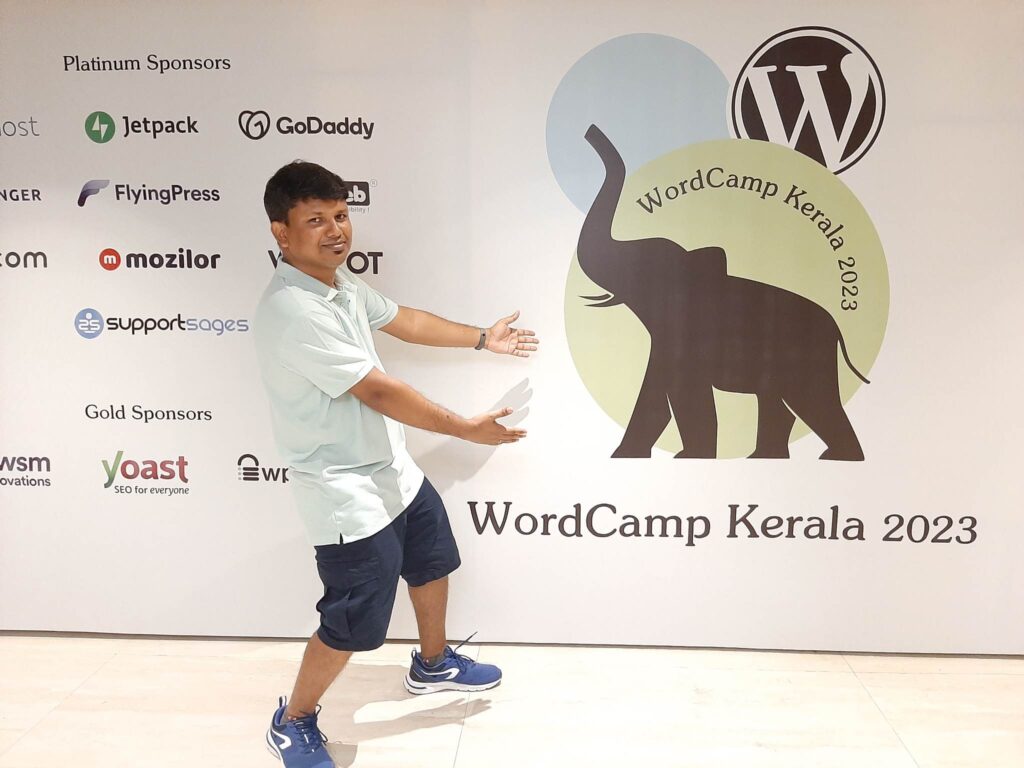 This is a photo of WebDevStudios Backend Engineer Lax Mariappan at WordCamp Kerala, as he poses in front of the event's backdrop.