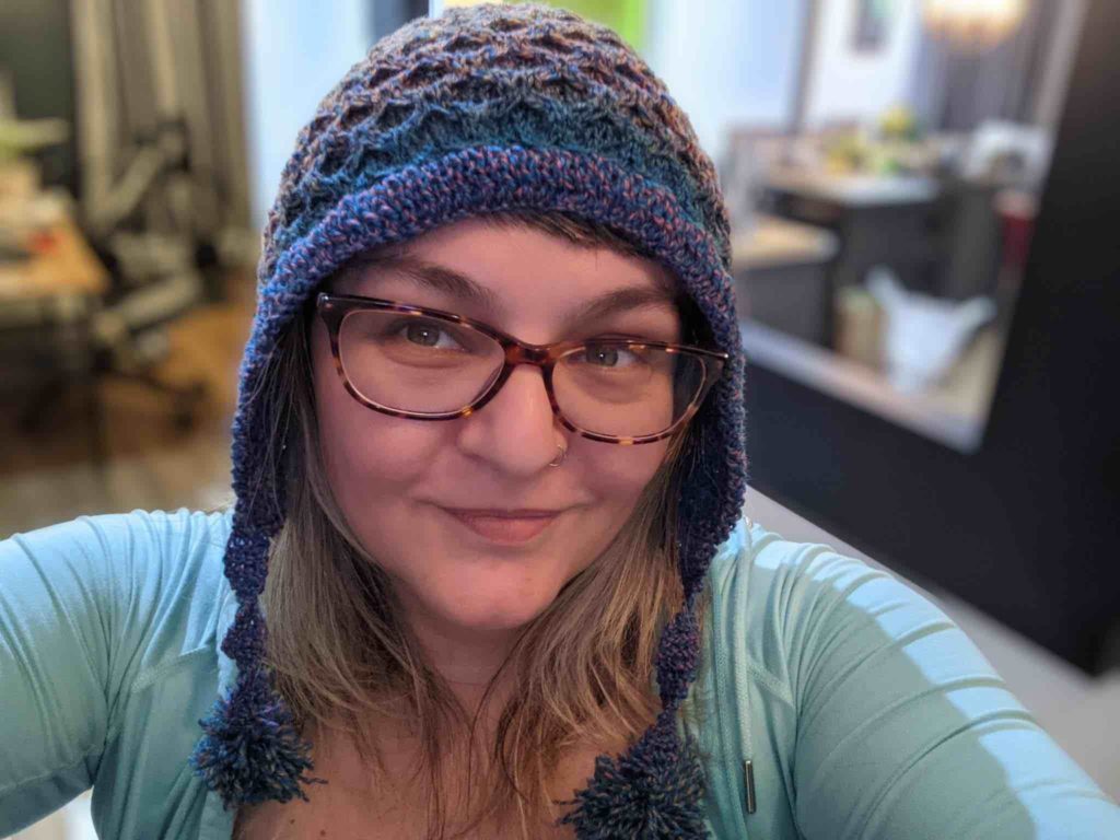 This is an indoor, selfie-style portrait of Inna Gutnik, a frontend engineer at WebDevStudios. She is smiling and wearing a navy and purple crocheted hat that she probably crocheted herself.