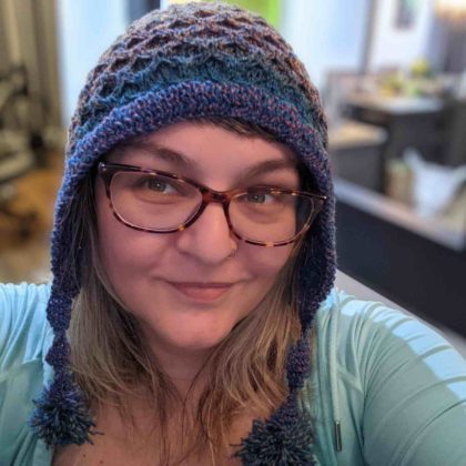 This is an indoor, selfie-style portrait of Inna Gutnik, a frontend engineer at WebDevStudios. She is smiling and wearing a navy and purple crocheted hat that she probably crocheted herself.