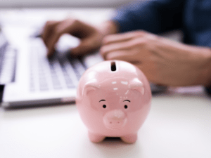 This is a photo of a pink piggy bank sitting next to someone at a laptop.