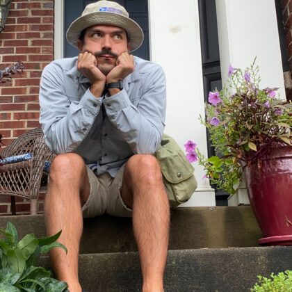 This is an outdoor portrait of Senior Project Manager Daniel Lama. He is wearing a hat and sitting on a porch.