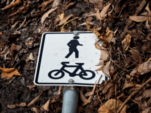 This is a photo of a trail sign with bicycle and pedestrian icons on it. The sign has fallen over onto the trail, and it is used to convey how confusing WordPress jargon can be.