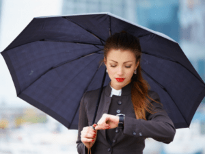This is an outdoor photo of a woman holding an umbrella while looking at her watch.