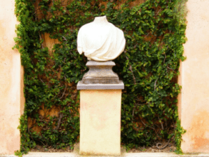 This is an image of a headless bust in front of a wall covered with vines.