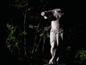 This is a headless statue in a wooded area at night.