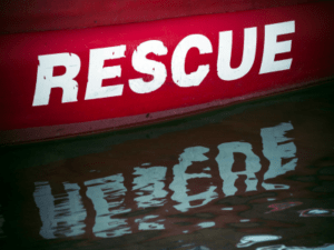 The word rescue painted in white on the red background of a boat floating in water. Rescue is reflected in the water.